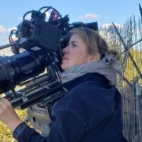 Cinematographer operating a professional camera outdoors beside a fence