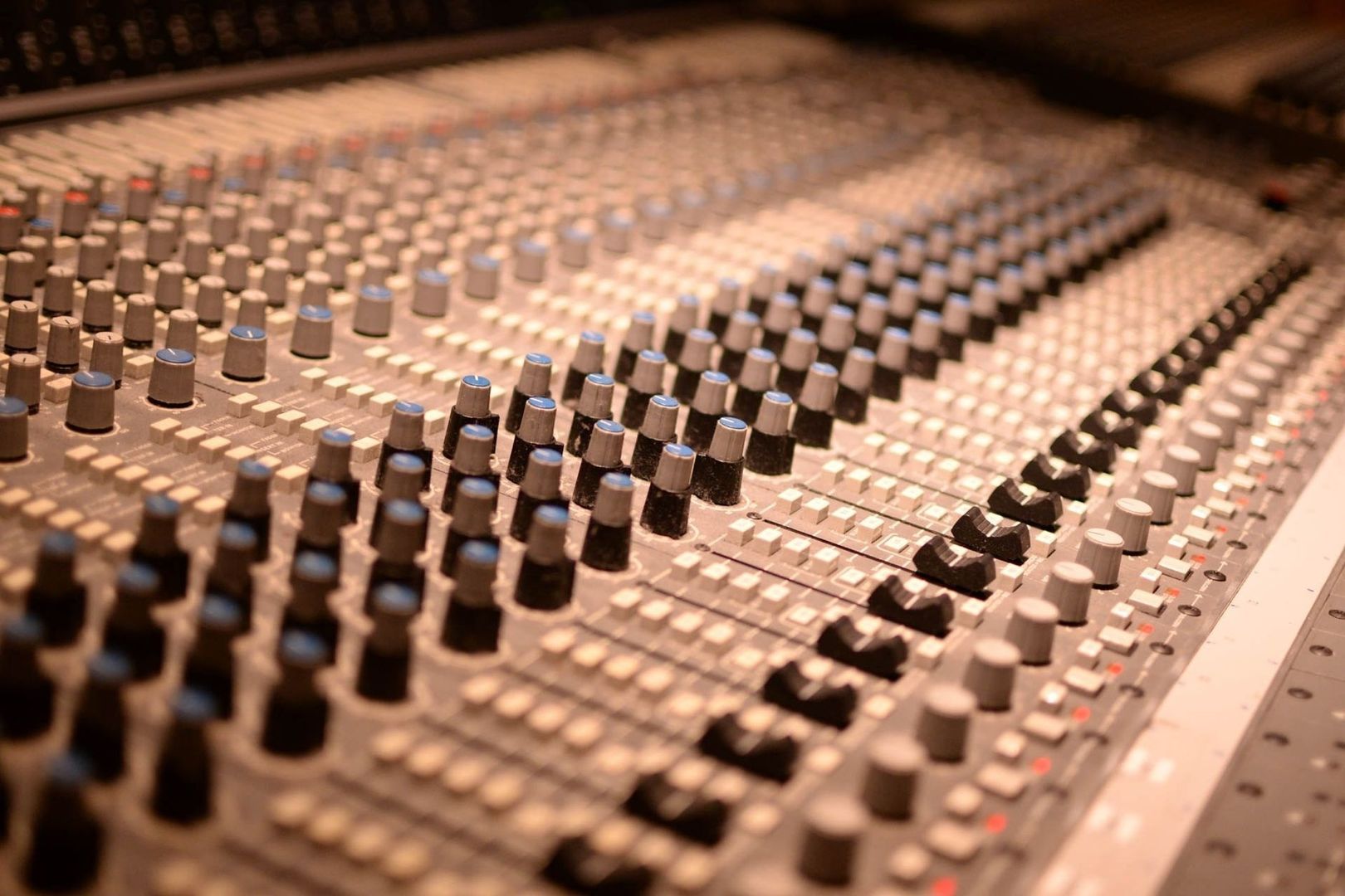 Close-up of an audio mixing console with rows of knobs and sliders