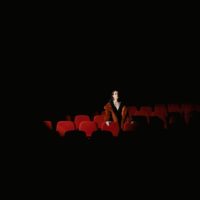 A lone woman sits among red cinema seats in a dark theater