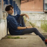 Contemplative young person sitting beside a weathered urban building
